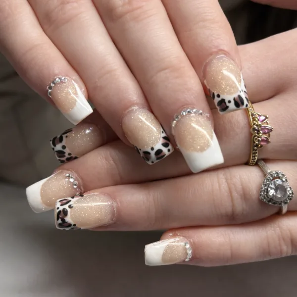 A soft champagne shimmer base paired with a crisp white french tip, finished with delicate leopard detailing and subtle crystal accents.